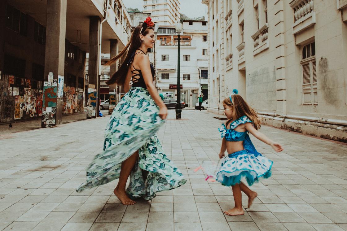 Босая девушка в цветастой юбке танцует на улице вместе с маленькой девочкой