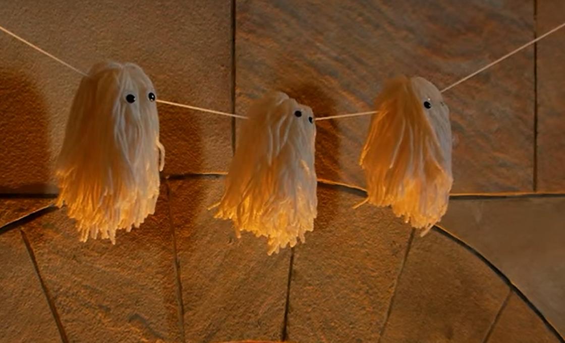 Забавные привидения, сделанные из вязальных ниток, висят на веревке над камином