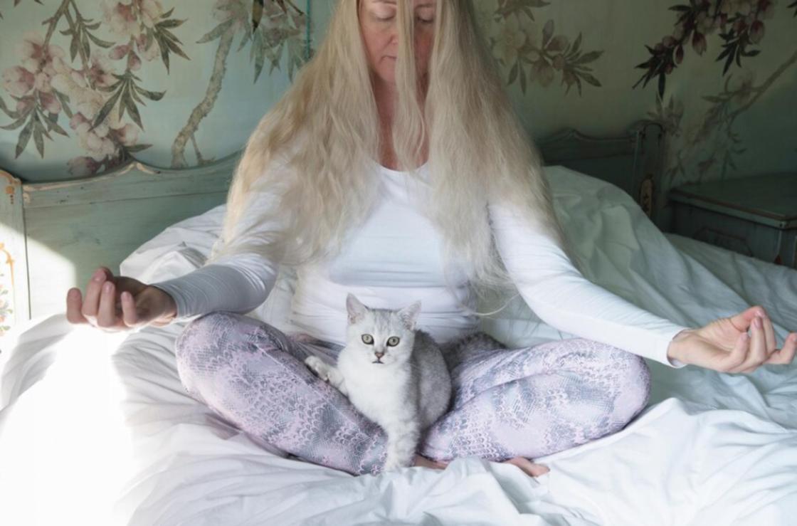 Женщина медитирует с кошкой в ногах