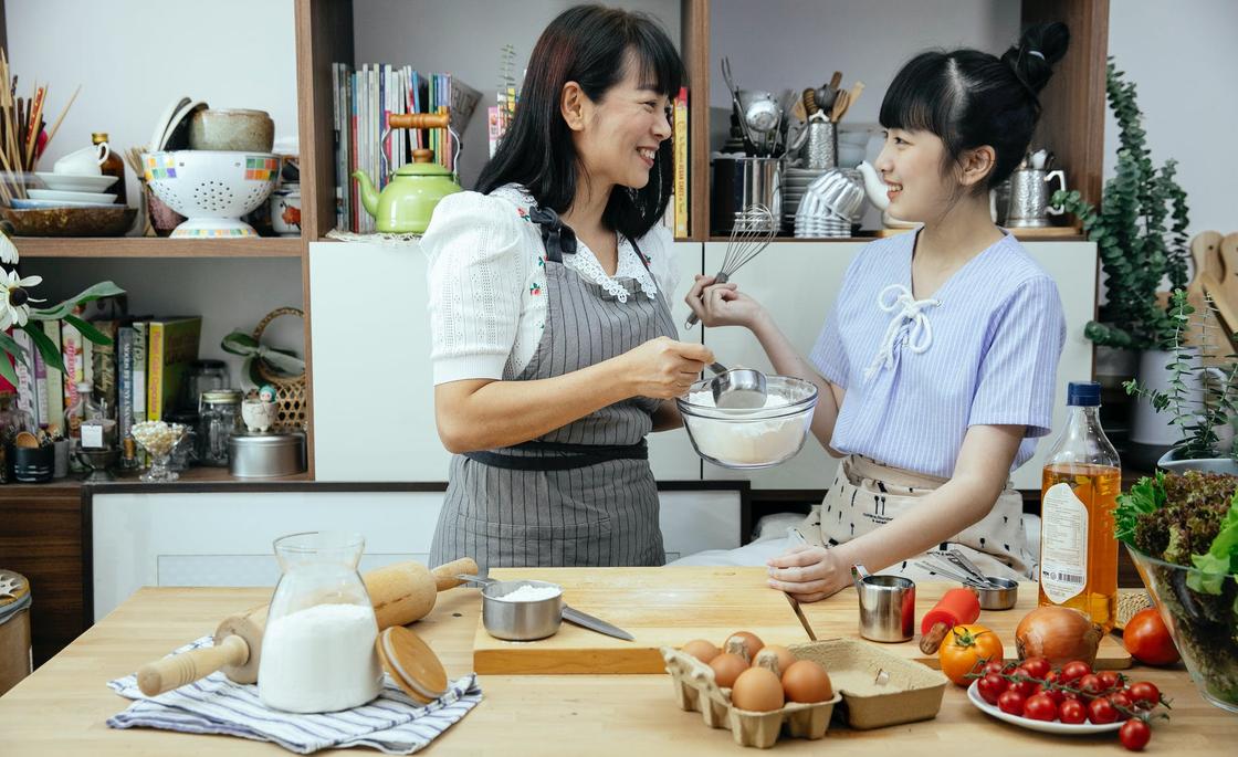 Молодая девушка готовит еду вместе с матерью и улыбается