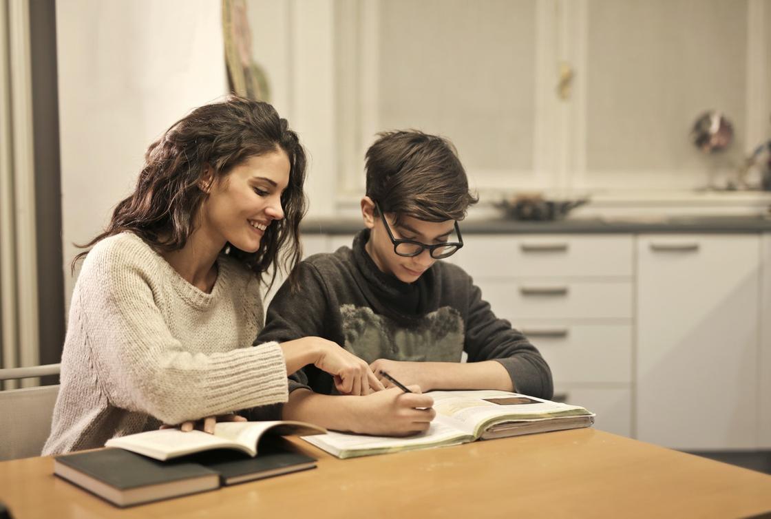Мама с ребенком сидят за столом и вместе делают уроки