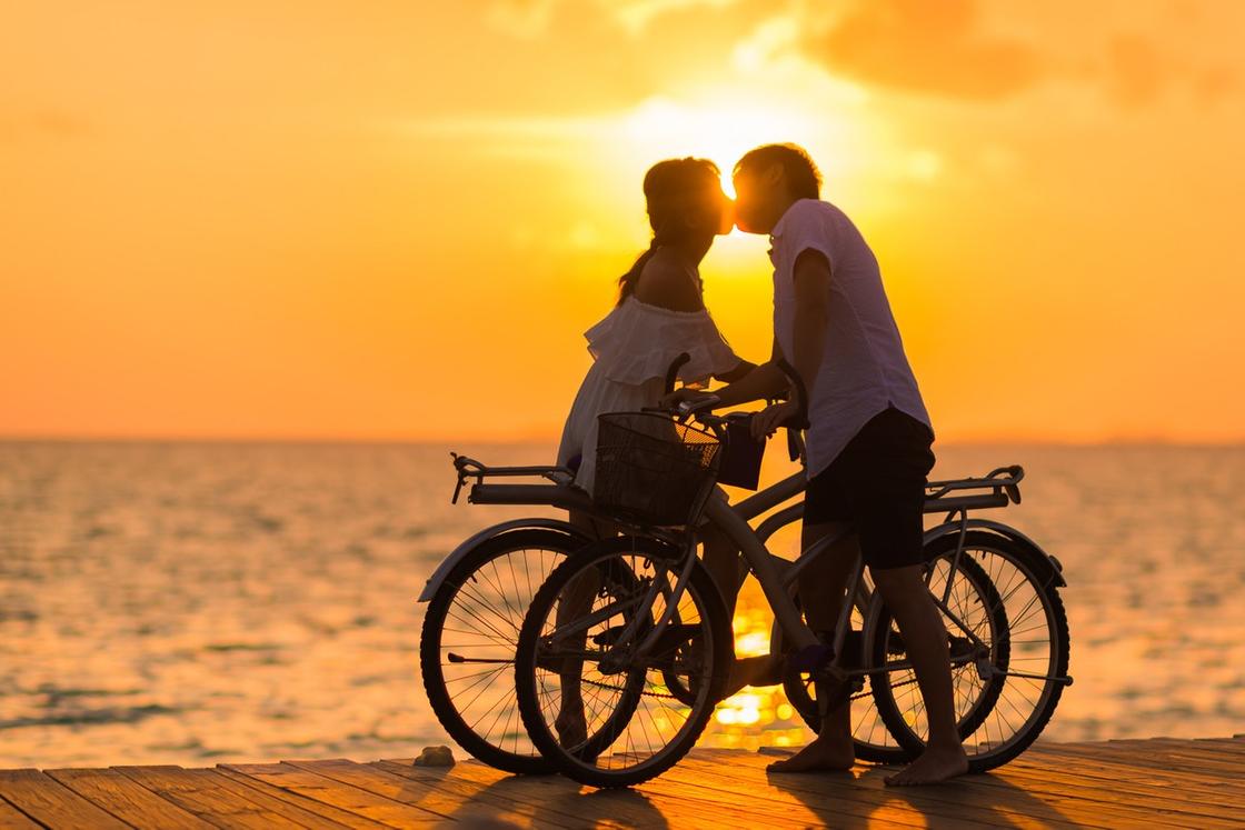 Мужчина и женщина целуются на фоне заката, стоя возле велосипедов