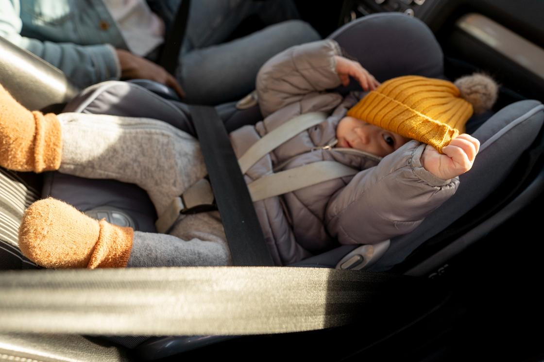 Маленький ребенок в автолюльке, установленной на сиденье автомобиля и пристегнутой ремнем безопасности