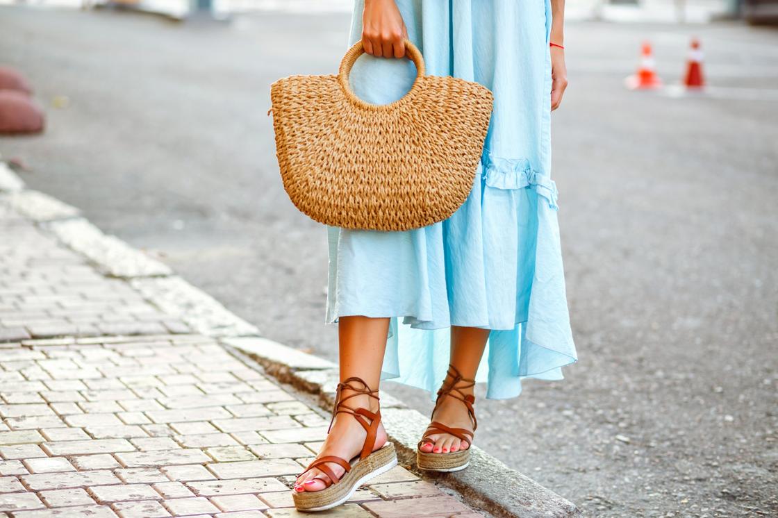 Девушка в голубом платье и летней обуви держит плетеную сумку