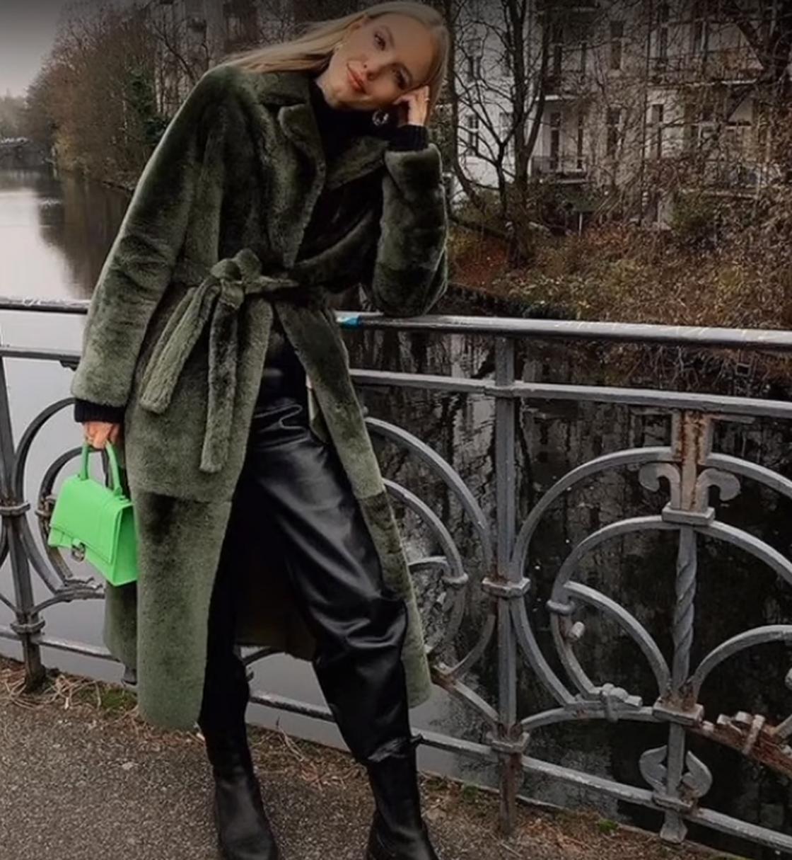Девушка в оливковой шубе, кожаных брюках держит зеленую сумку