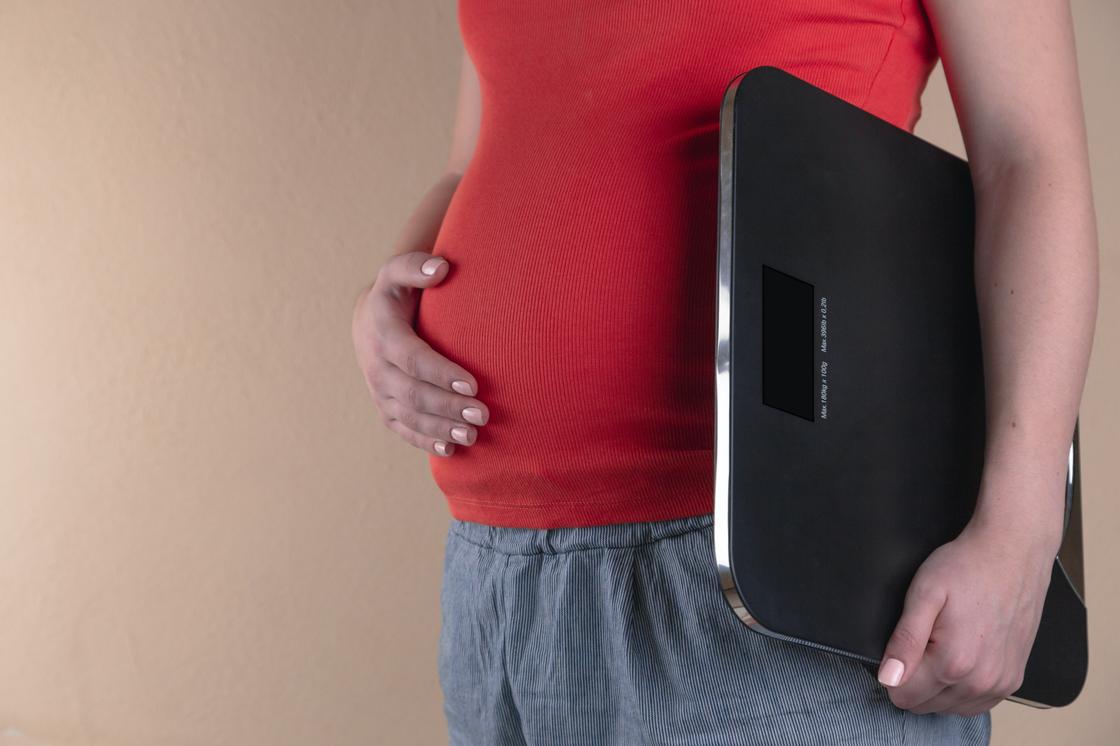Беременная женщина держит в руках напольные весы