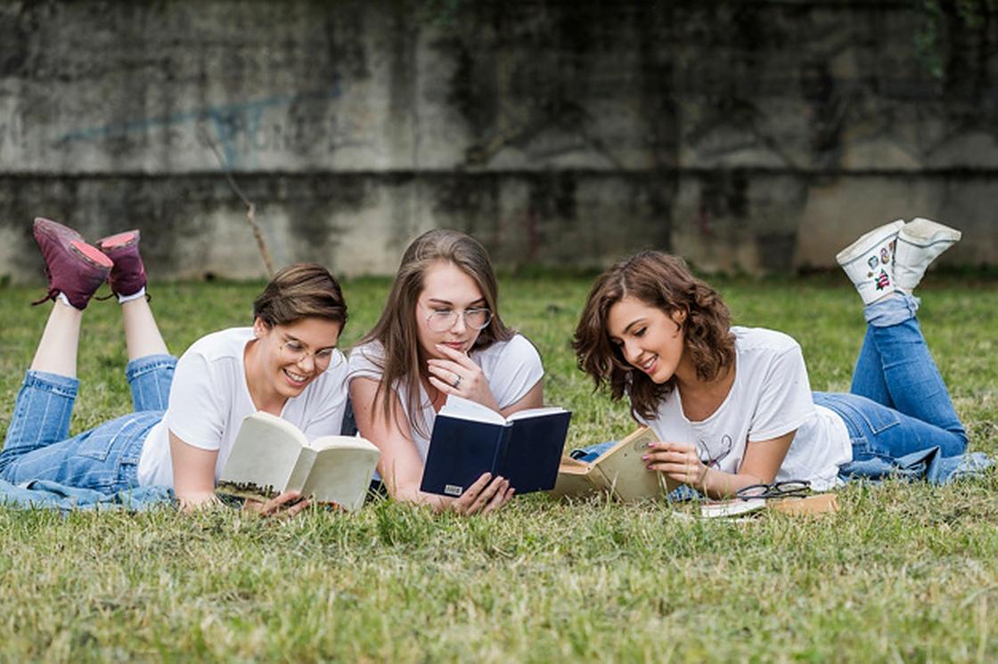 Три девушки читают книги лежа на траве