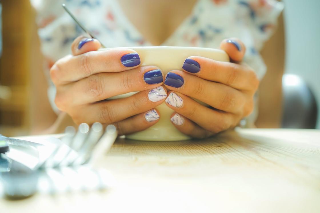 Женские руки с маникюром в белых и синих цветах держат чашку