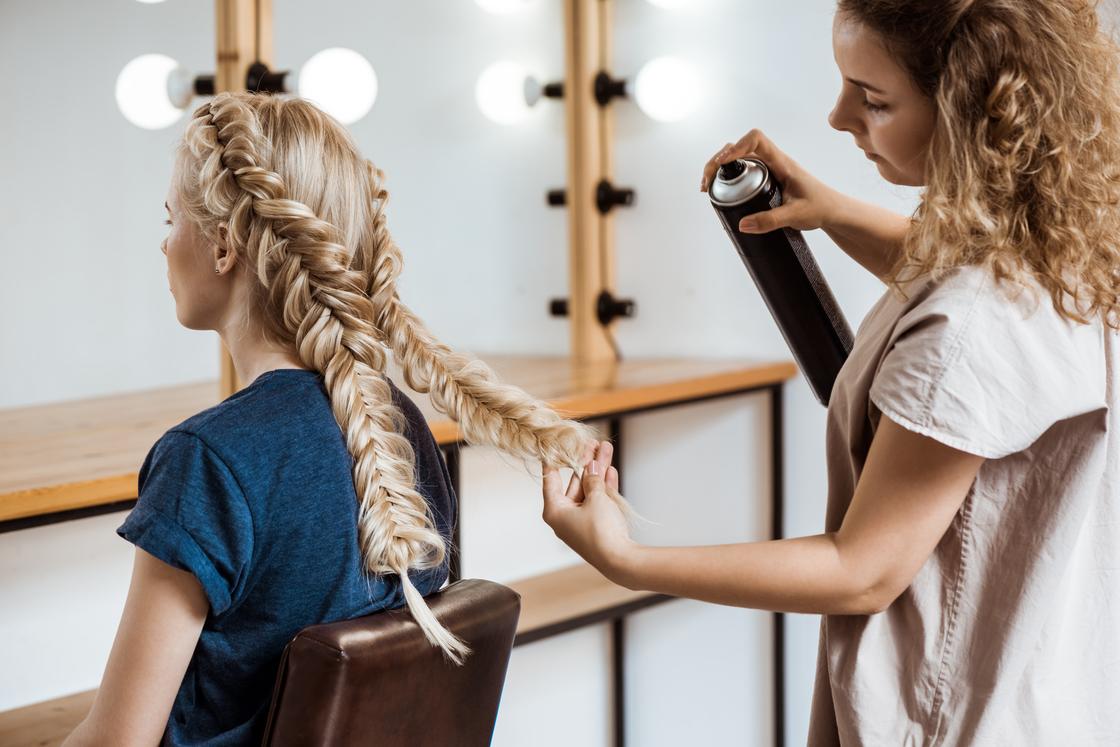 Парикмахер делает девушке прическу с косами