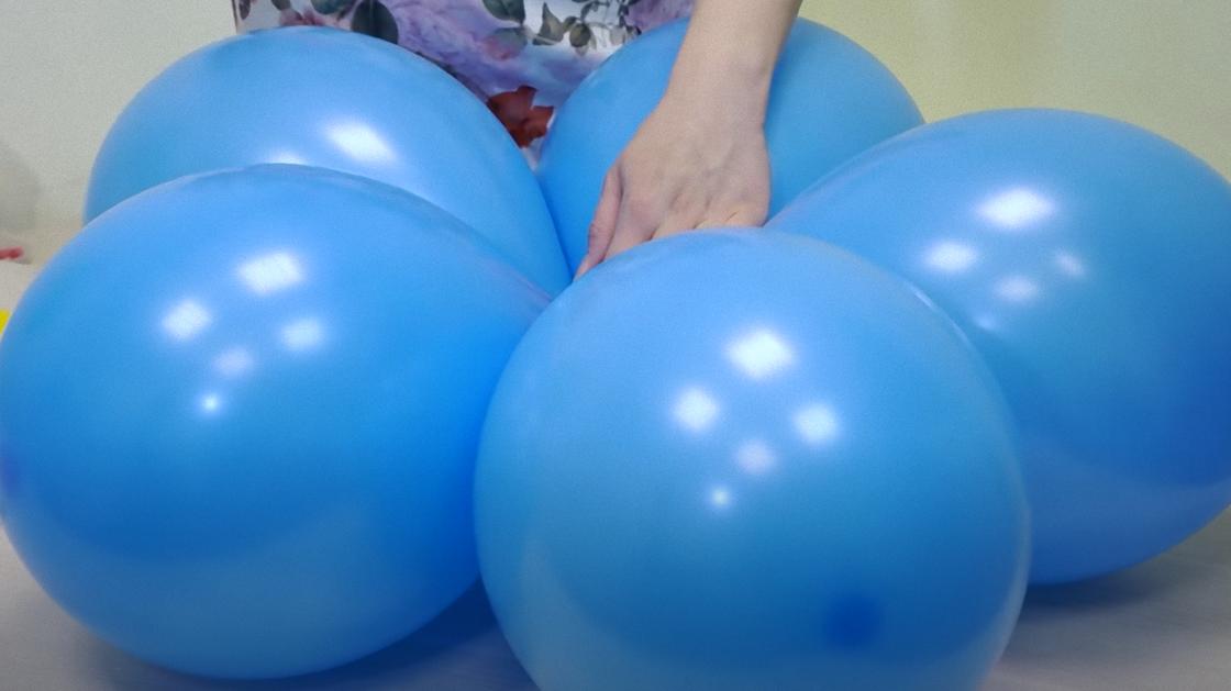 На столе лежат надутые синие шары, соединенные вместе в виде цветка. Их придерживают рукой по центру