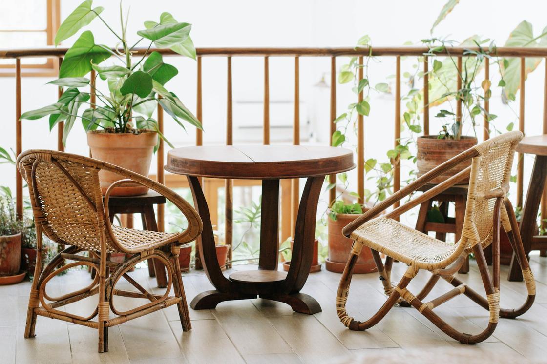 На открытом балконе плетеные кресла, деревянный стол, кашпо с цветами