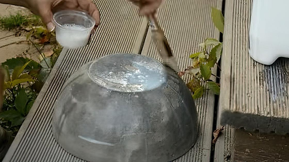 Бетонную чашу перевернули на ровной доске и смазывают щеткой, смачивая в жидкости, налитой в небольшую емкость