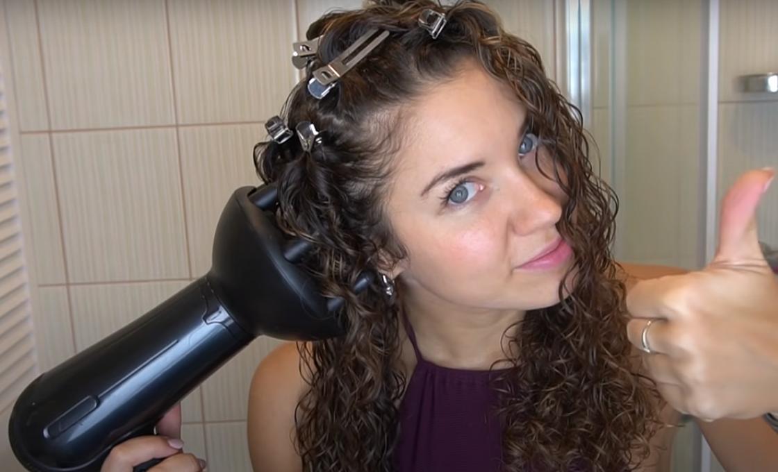 Кудрявая девушка использует диффузор для сушки волос феном