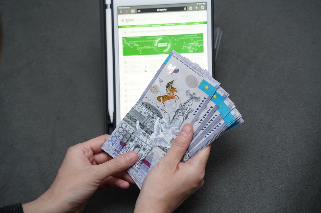Женщина держит пачку денег на фоне планшета