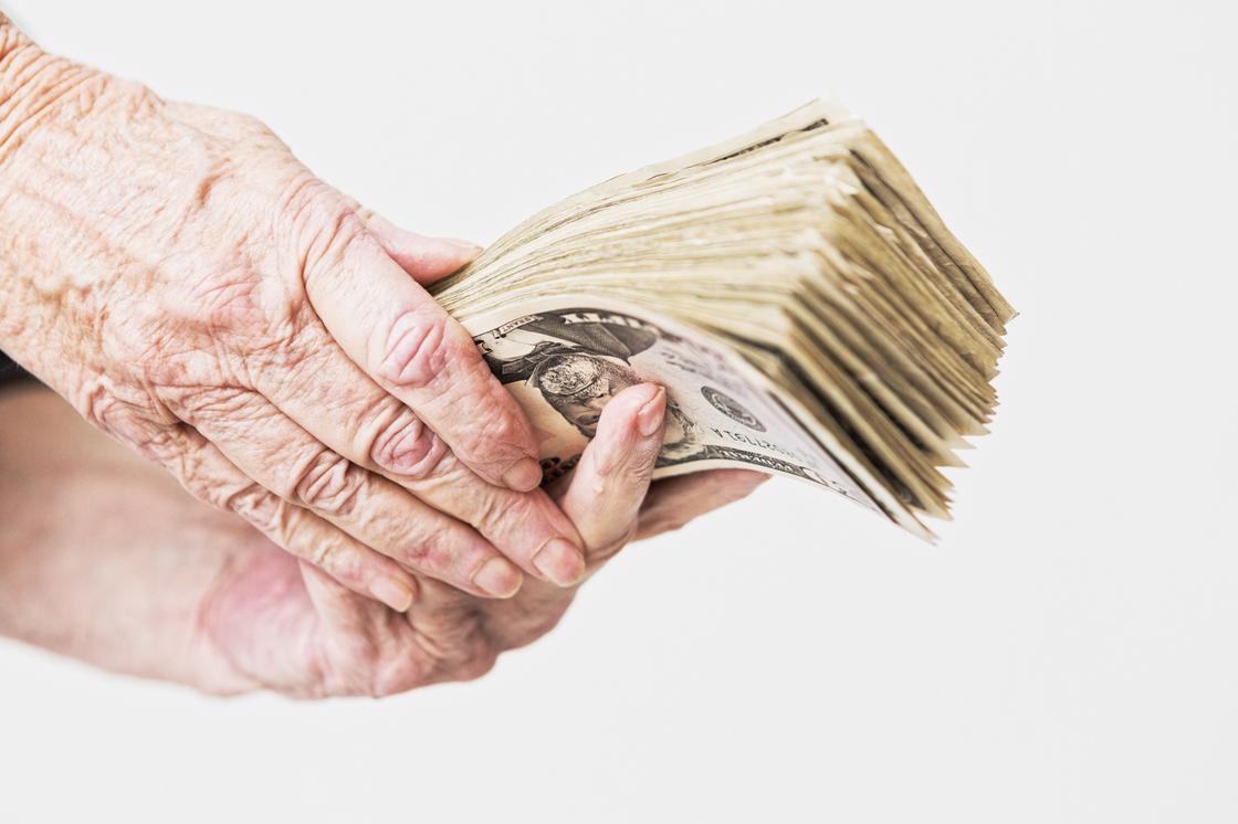 Пенсионерка держит в руках много денег
