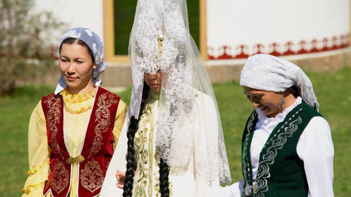 Женщины поддерживают под руки невесту. На голове у невесты белый платок