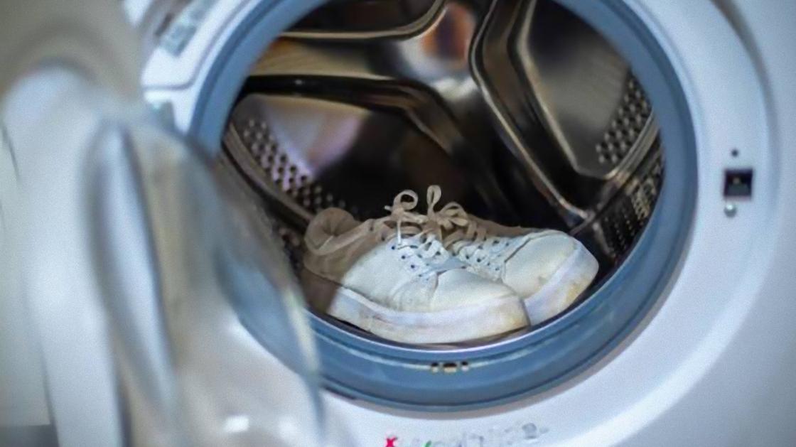 Белые кроссовки лежат в открытом барабане стиральной машины