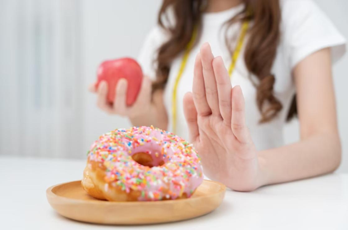 Девушка делает отрицающий жест рукой для тарелки с пончиком