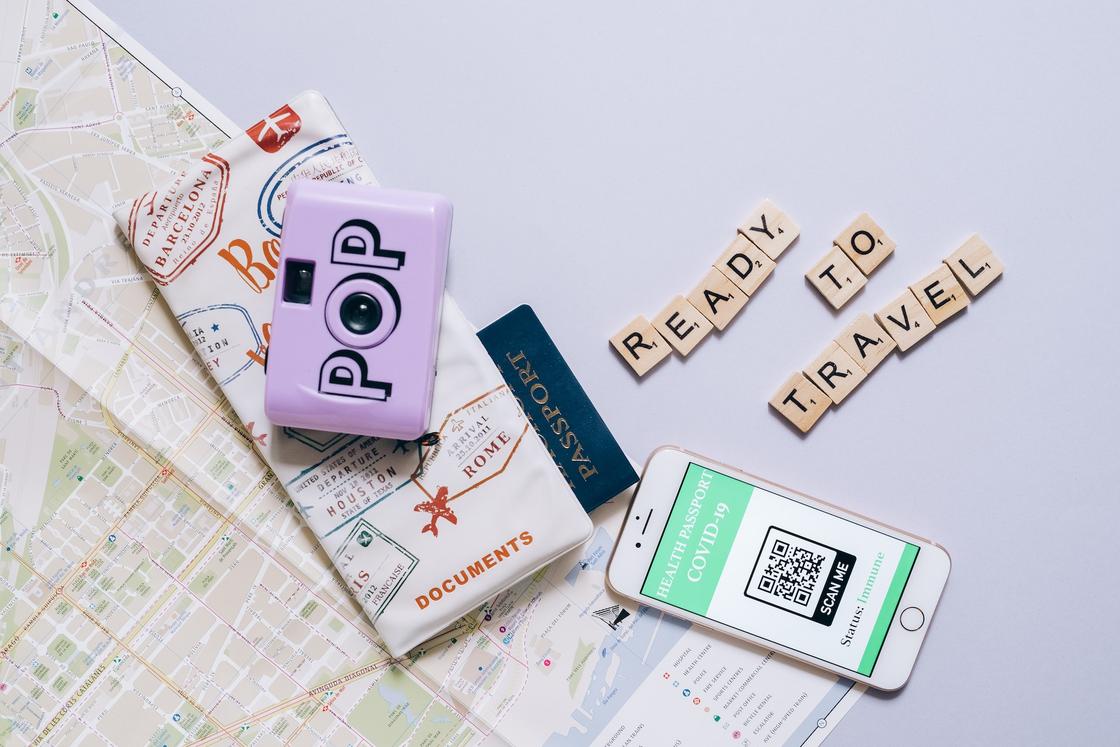 На карте лежит паспорт, фотоаппарат, телефон с QR-кодом и кубиками выложена надпись Ready to travel На карте лежит паспорт, фотоаппарат, телефон с QR-кодом и кубиками выложена надпись Ready to travel