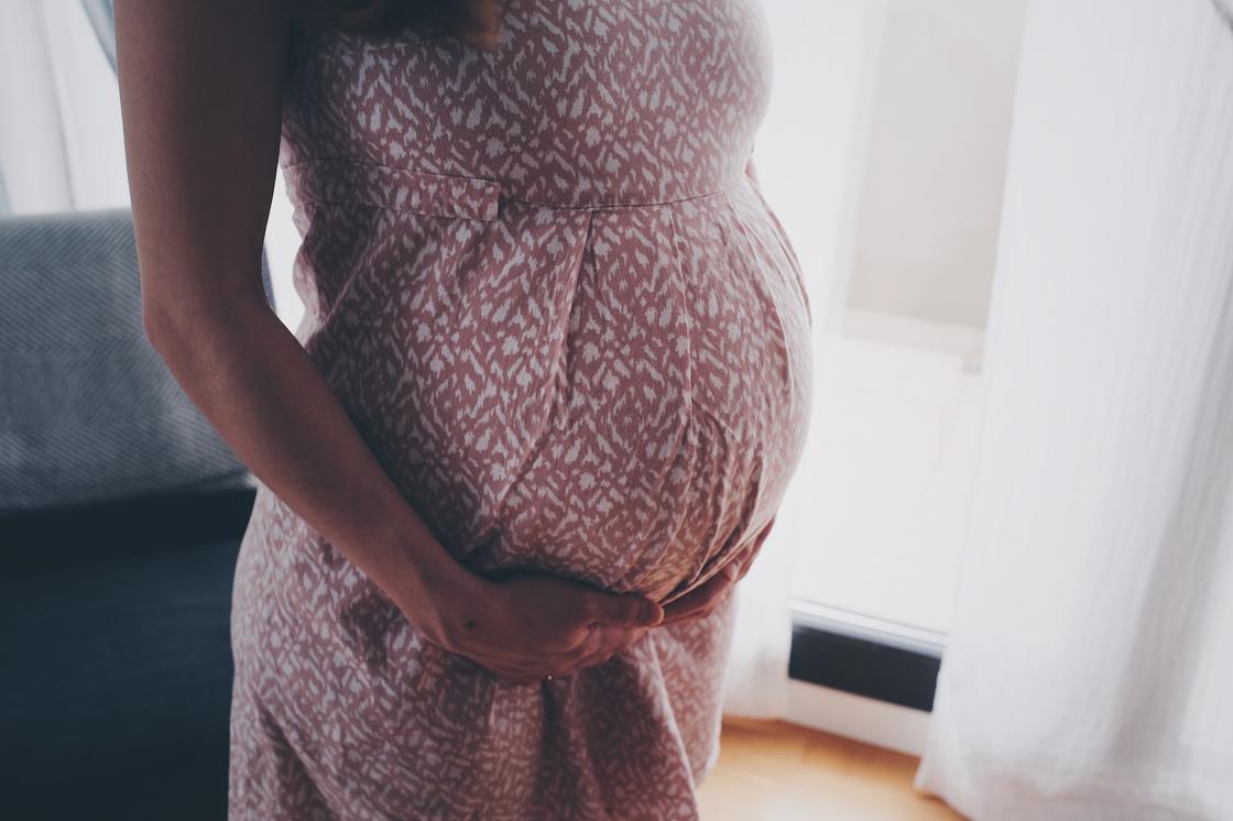 Беременная женщина поддерживает живот руками