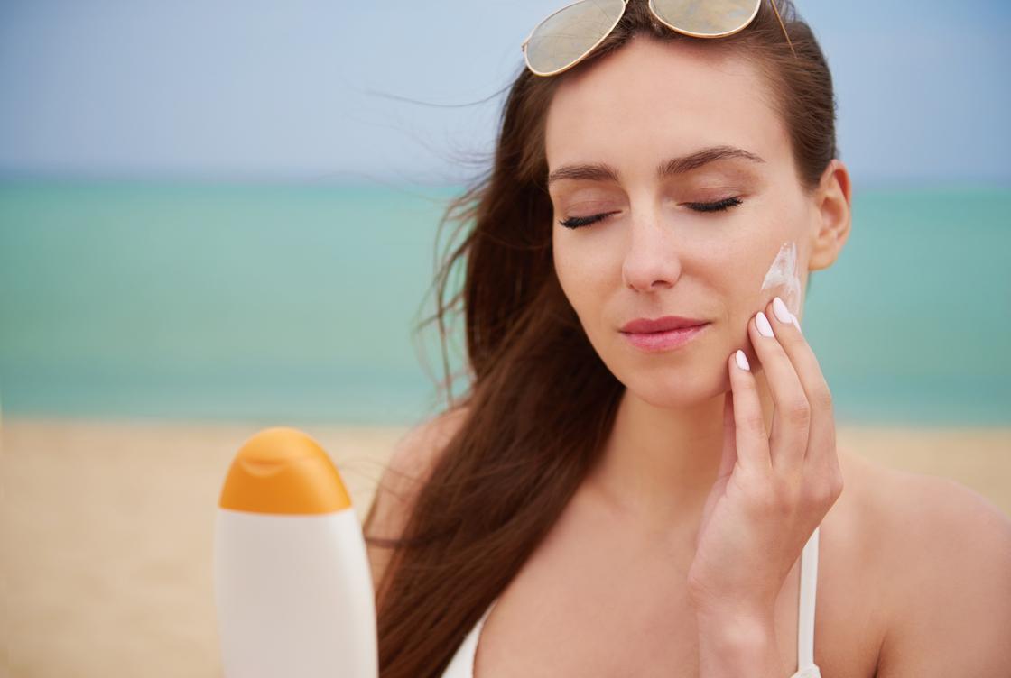 Девушка наносит солнцезащитный крем на пляже
