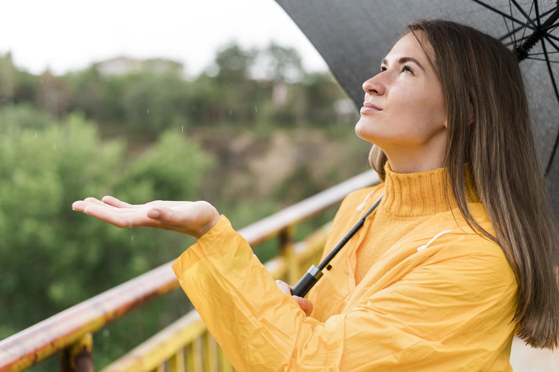 Девушка с зонтиком ловит капли дождя на ладони