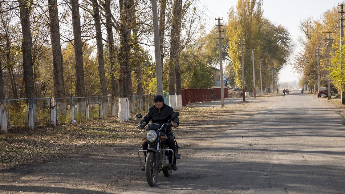 Мужчина едет по селу на мотоцикле