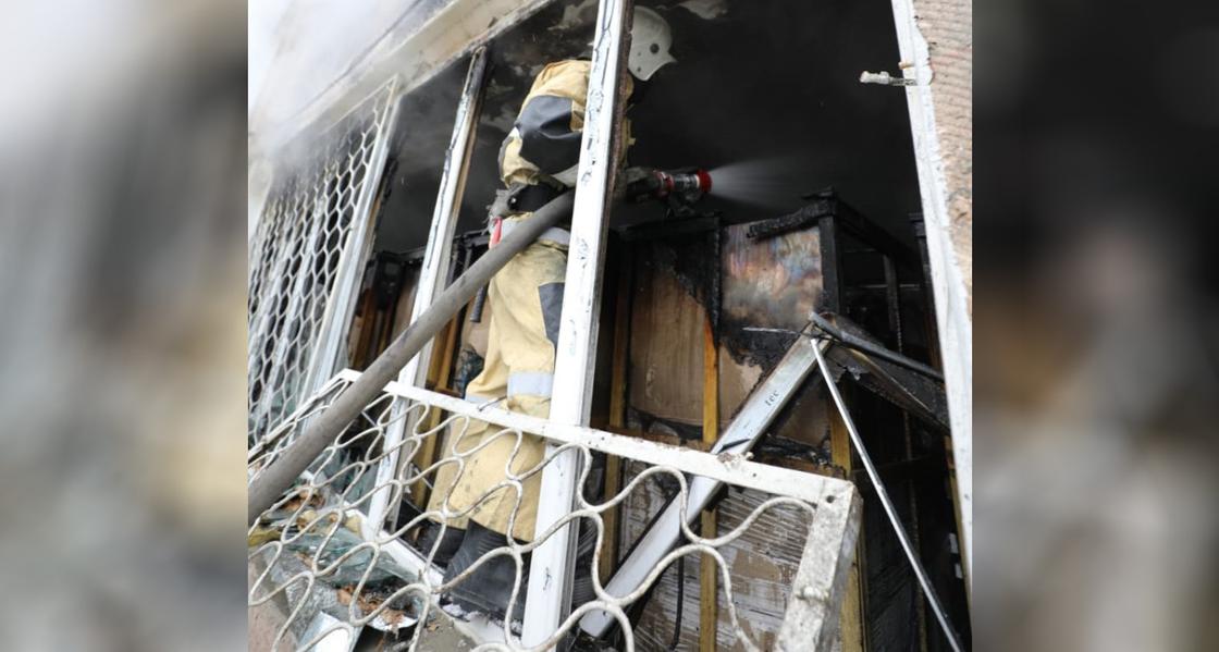 Пожарный тушит огонь, стоя в окне здания