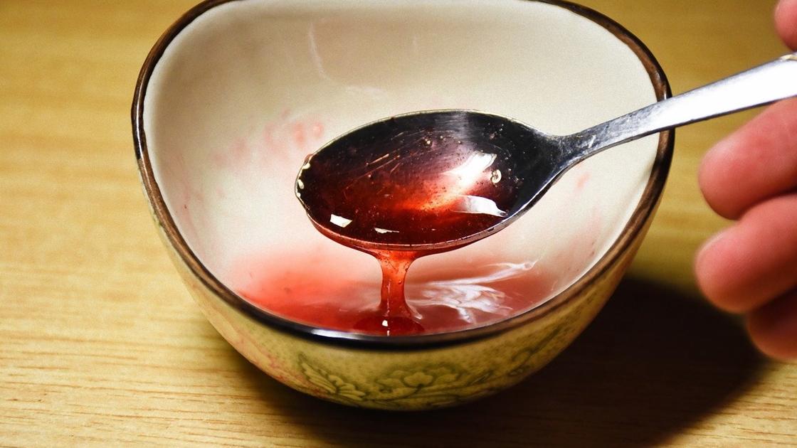 Ложкой набирают густой клубничный сироп из миски Ложкой набирают густой клубничный сироп из миски