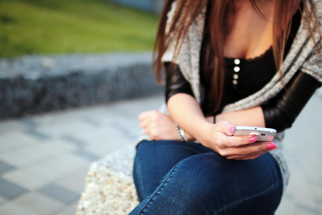 Девушка сидит на улице с телефоном в руках