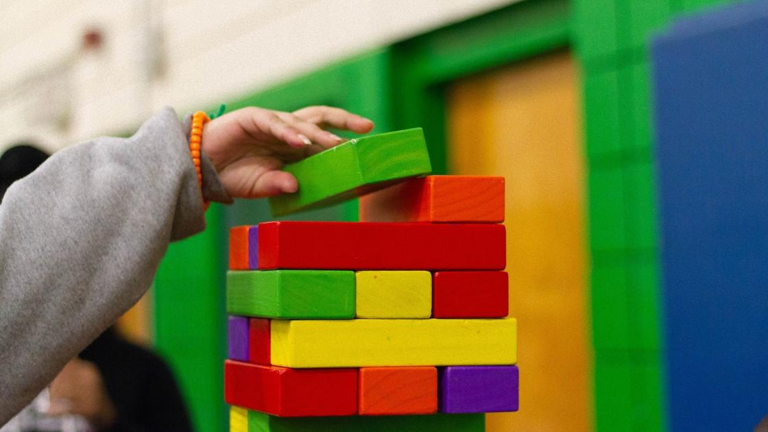 Рука ребенка складывает цветные детали деревянного конструктора в виде башни