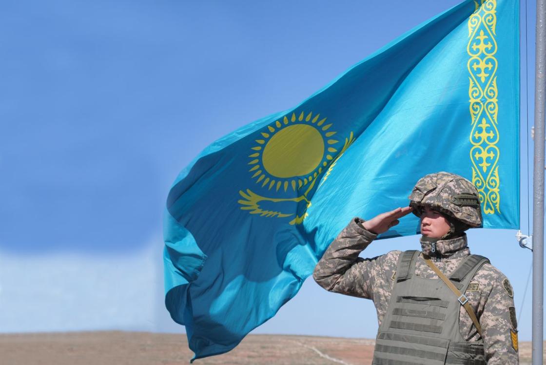 Казахстанский военнослужащий стоит возле флага Казахстана
