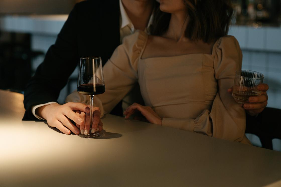 Мужчина и женщина обнимаются, сидя рядом с барной стойкой и держа винный бокал