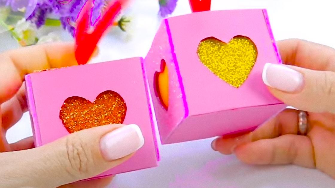 В руках держат две коробочки из розовой бумаги. Двойные подарочные коробочки с сердечками из фоамирана