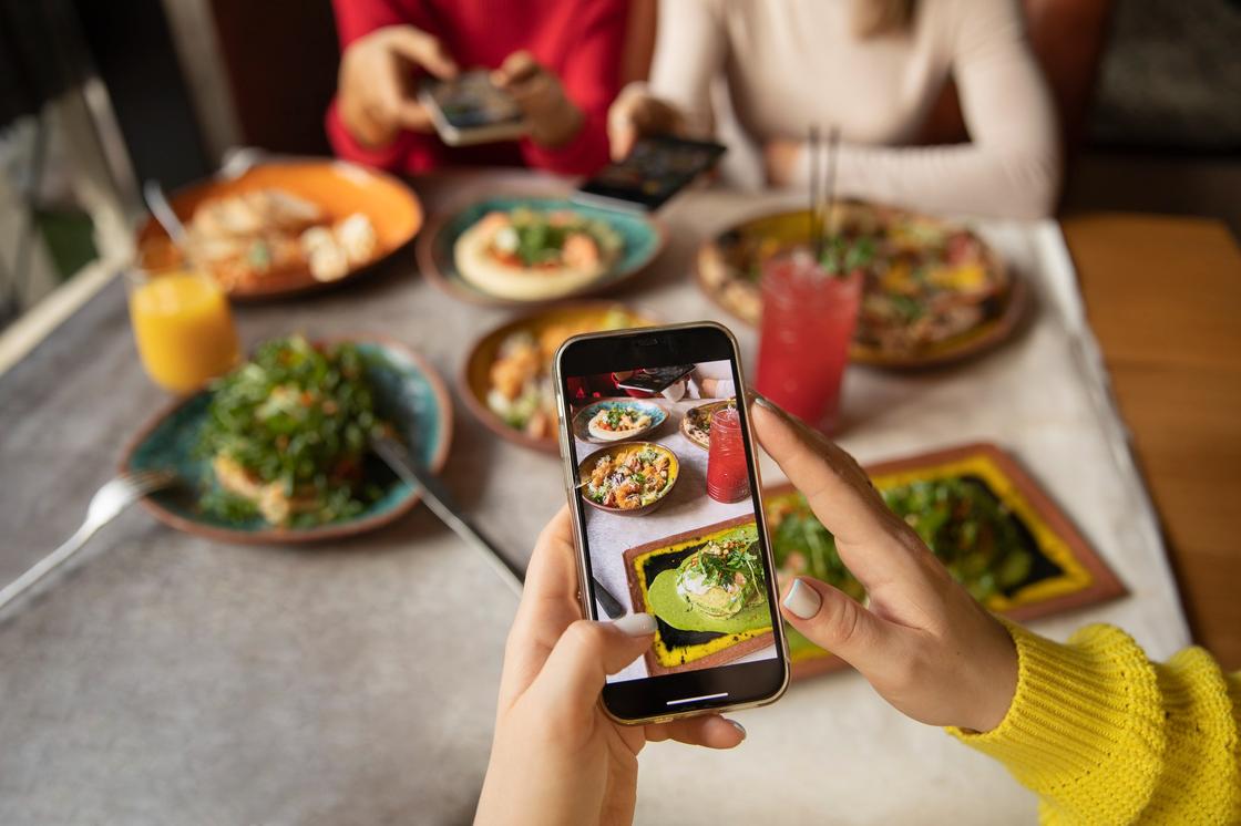 Женщина фотографирует ужин на смартфон