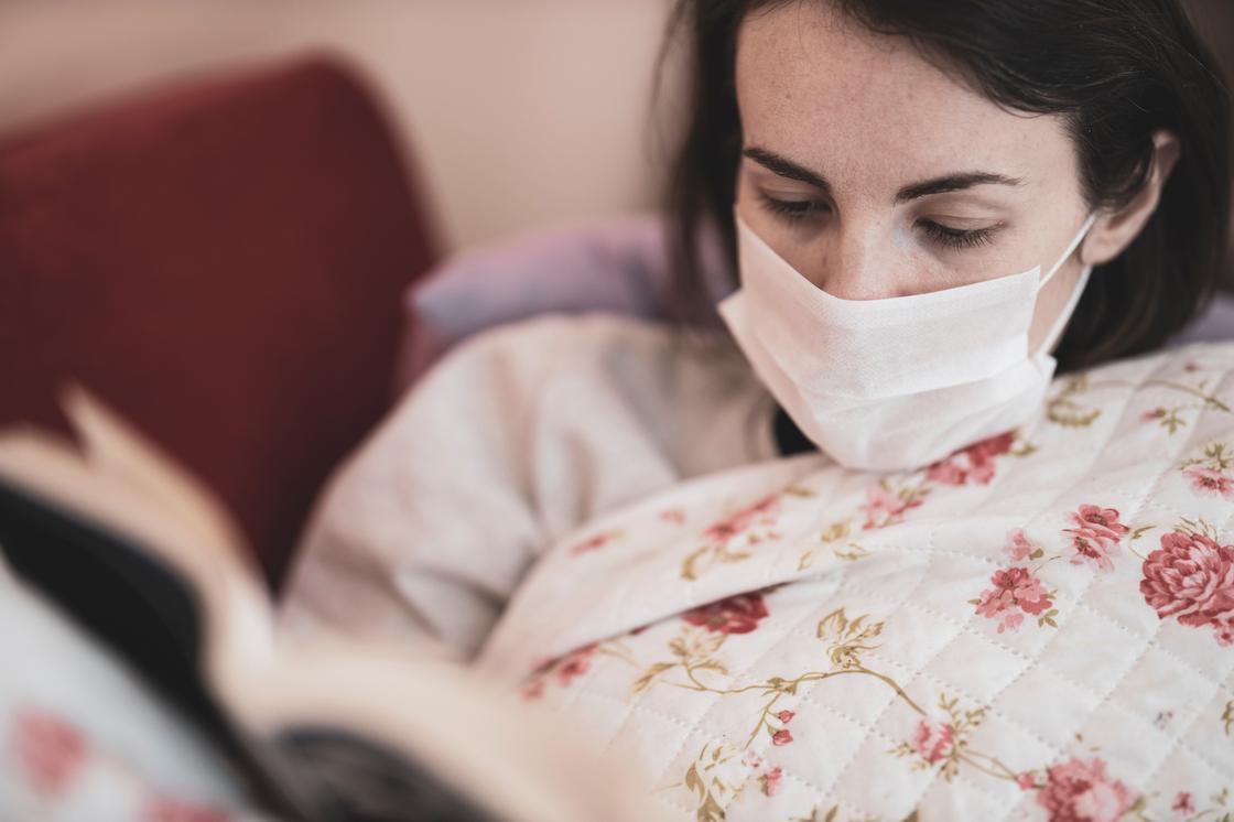 Девушка в медицинской маске читает книгу