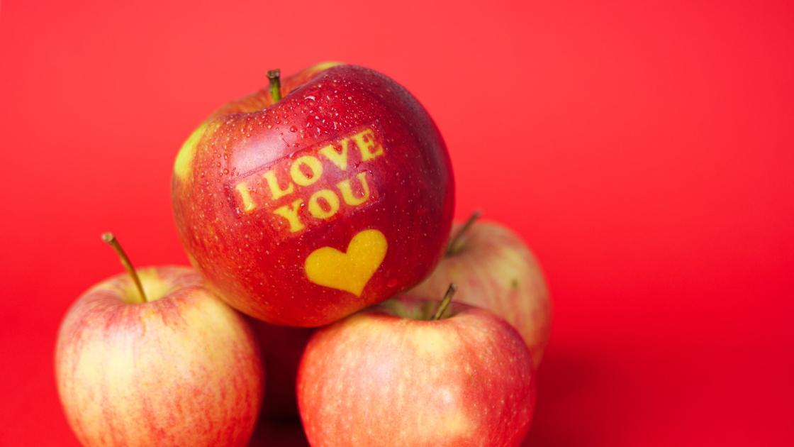 Красное яблоко с надписью на английском языке "я тебя люблю" на кучке других яблок