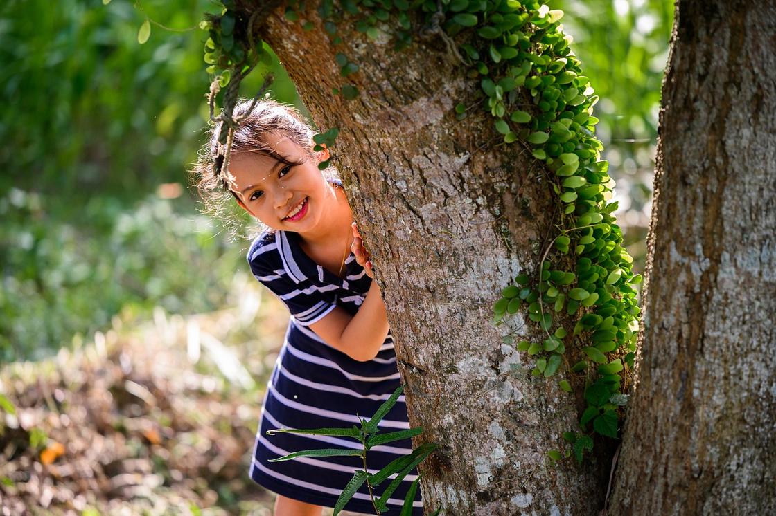 Девочка прячется за деревом