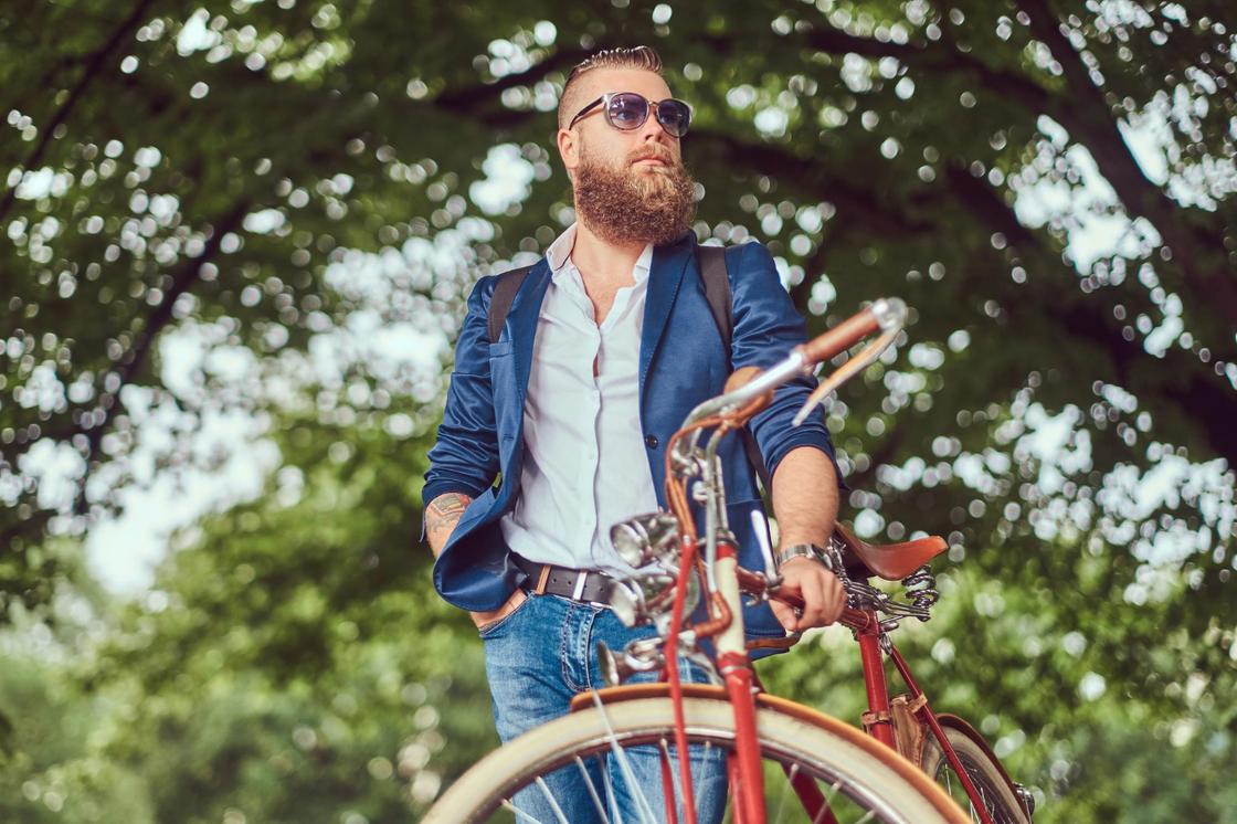Мужчина в хипстерской одежде с бородой держит велосипед