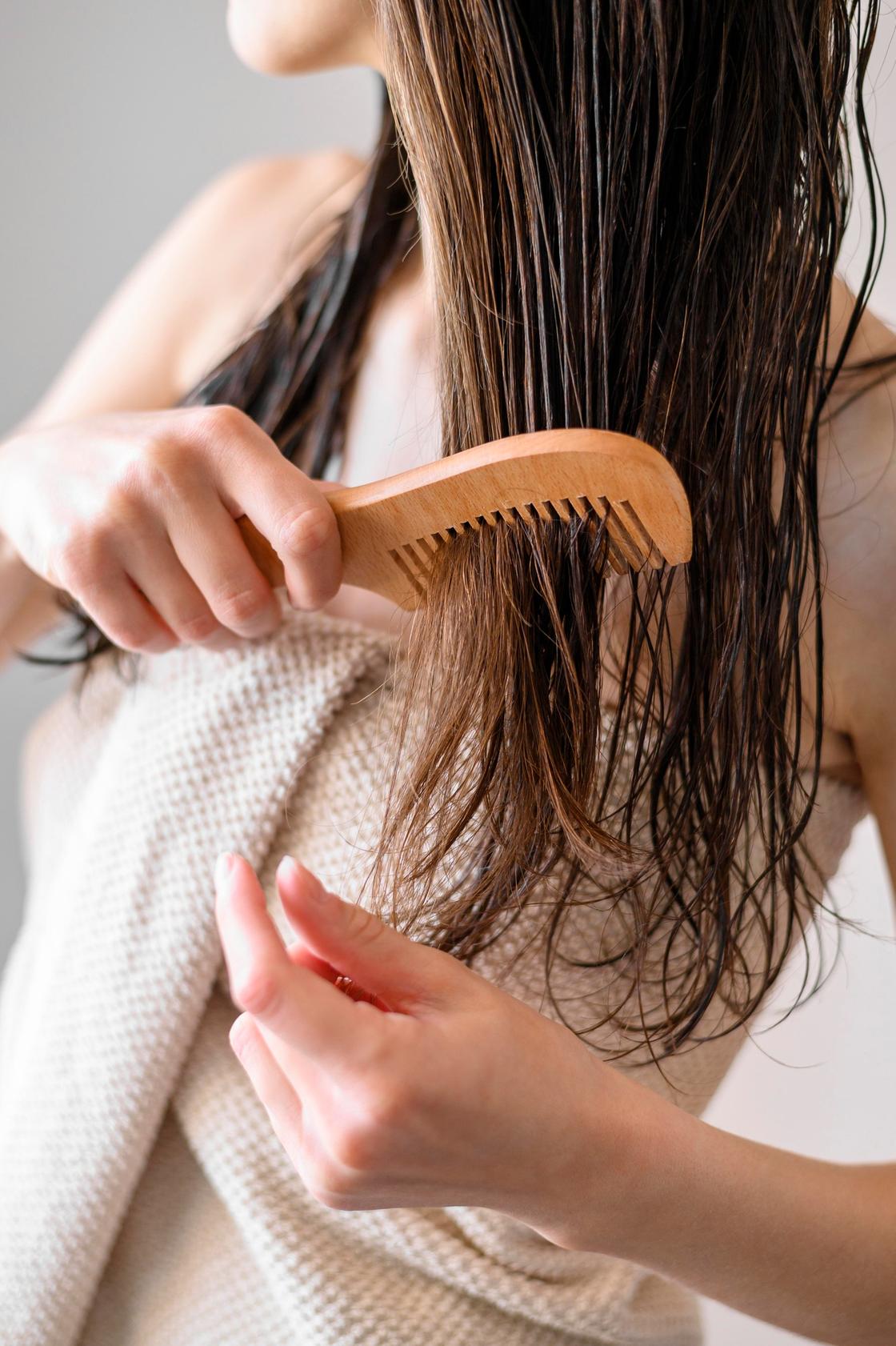 Девушка расчесывает длинные волосы деревянным гребнем с редкими зубьями