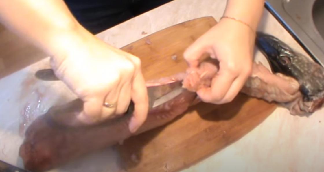 Женщина подрезает плавник щуки ножницами