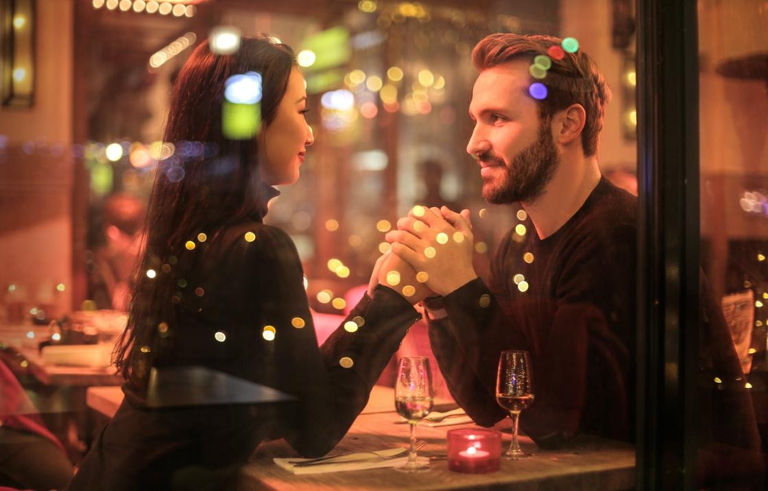 Мужчина и женщина держатся за руки, сидя за столиком в кафе