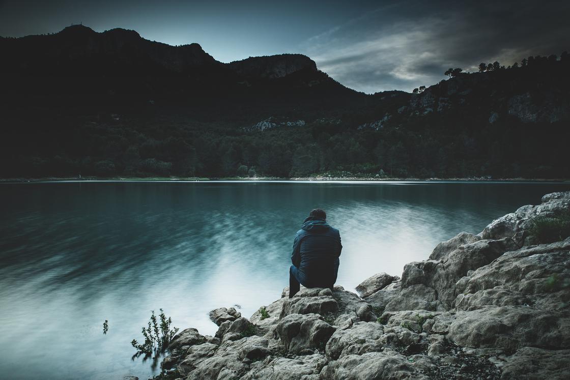 Мужчина сидит на берегу горного озера