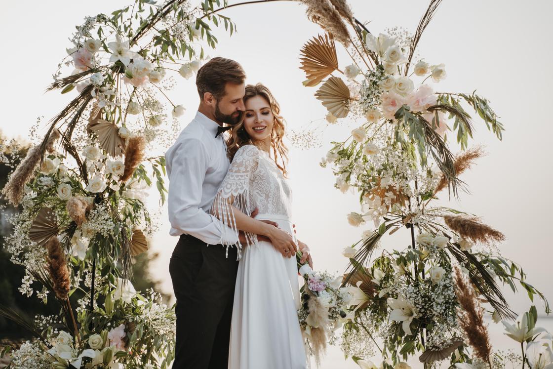 Свадьба в бохо-стиле: жених и невеста возле свадебной арки, украшенной свежими цветами и сухоцветами