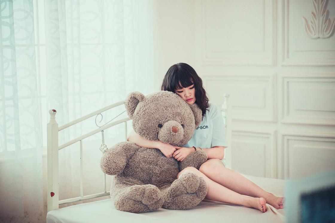 Девушка сидит на кровати, обнимая игрушечного медведя
