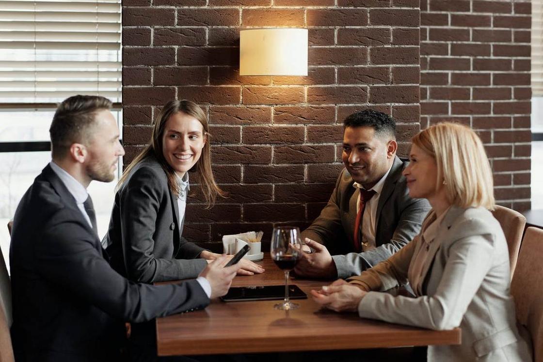 Четверо людей в деловых костюмах общаются, сидя за столиком в ресторане