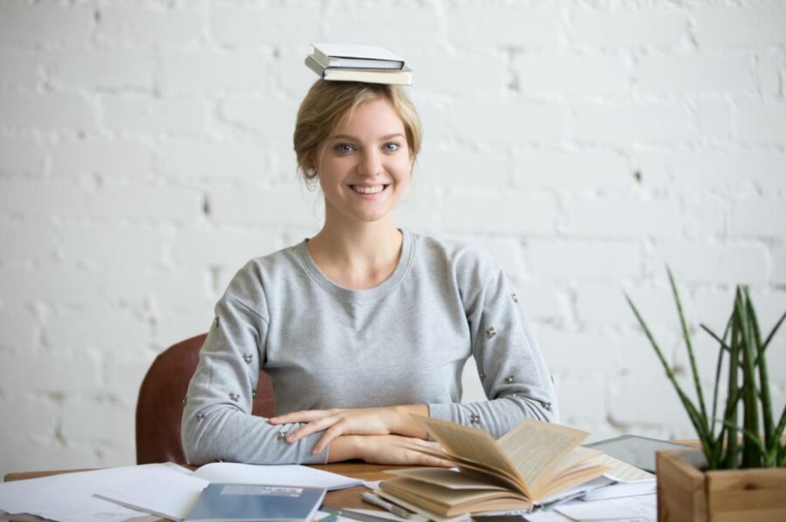 Женщина сидит за столом с книгами на голове