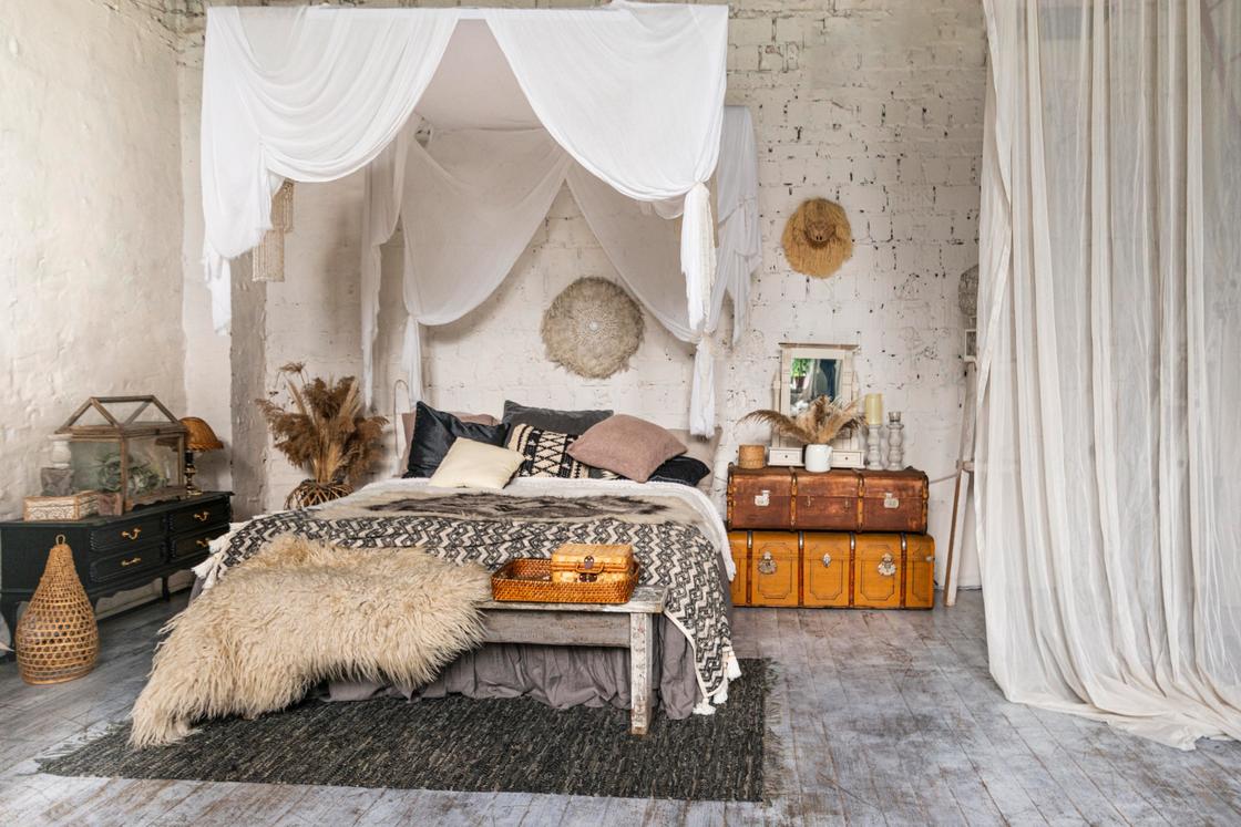 В комнате с кирпичными стенами расположена кровать, старинные чемоданы, балдахины из натуральных тканей
