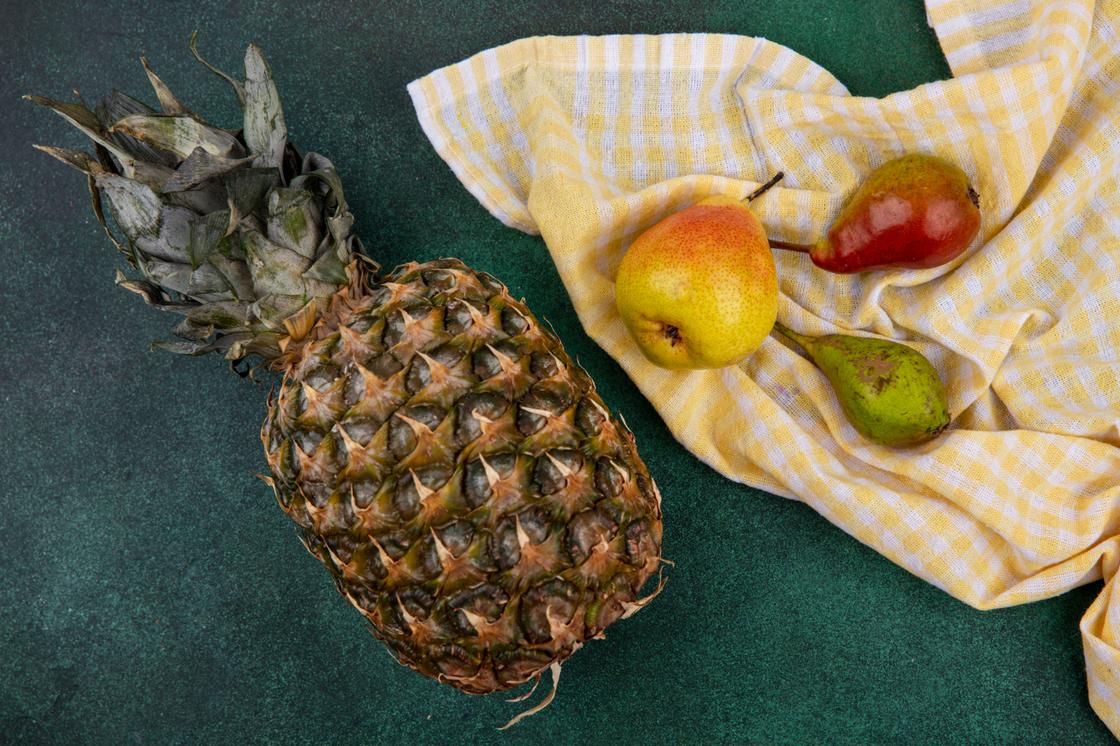На столе ананас и груши, выложенные на кухонном полотенце