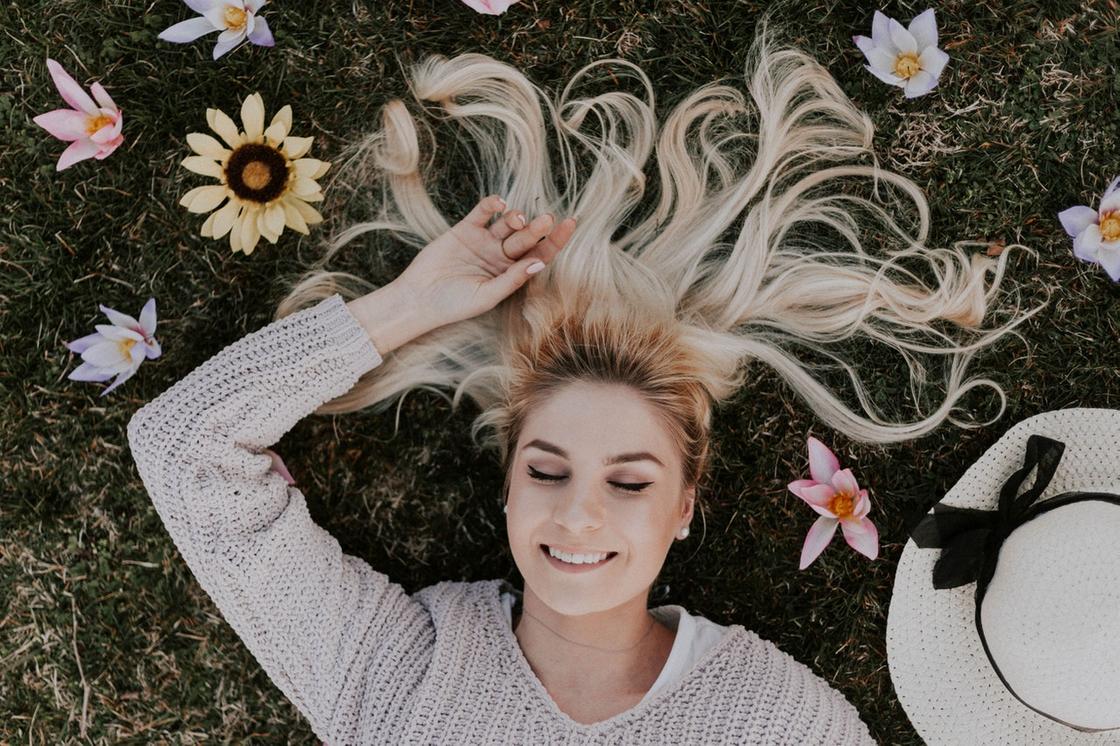 Девушка с белокурыми волосами лежит на траве среди цветов